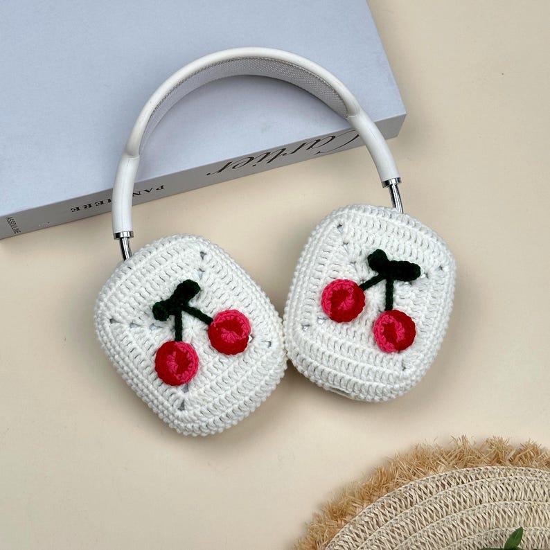 Pode incluir: Fones de ouvido brancos com desenhos de cerejas de croch&ecirc; nas conchas. As cerejas s&atilde;o vermelhas com caules verdes, em fundo branco. A faixa de cabe&ccedil;a &eacute; branca, dando um aspeto artesanal e decorativo.