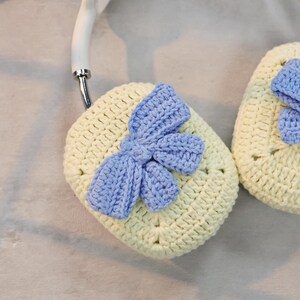 May include: Two crocheted headphone covers with a light blue bow on each. The covers are cream colored and the bows are a light blue.