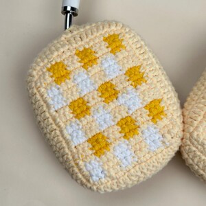 May include: Handmade crochet potholder in a light yellow color with a checkered pattern of yellow and white squares. The potholder is made of soft yarn and has a rounded shape. The potholder is designed for kitchen use.