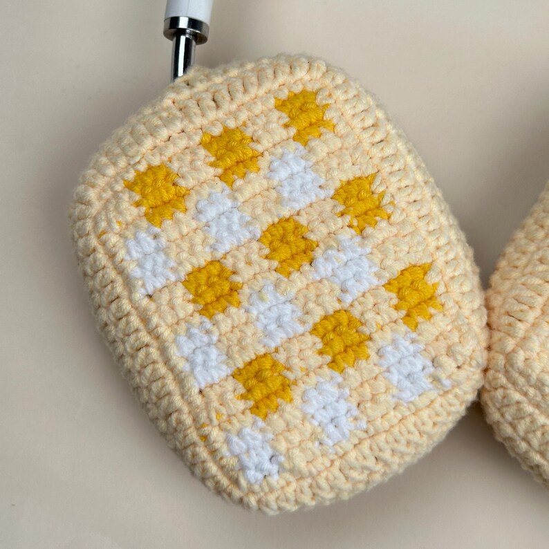 May include: Handmade crochet potholder in a light yellow color with a checkered pattern of yellow and white squares. The potholder is made of soft yarn and has a rounded shape. The potholder is designed for kitchen use.
