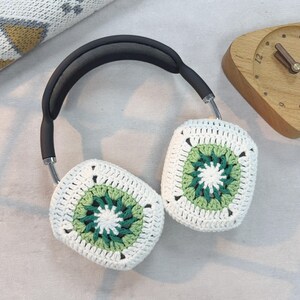 May include: White crocheted headphone covers with green and white geometric patterns. The covers are attached to a black headband.