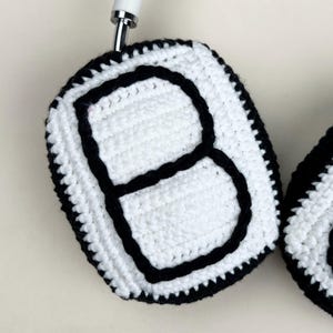 Peut inclure: Caches d'&eacute;couteurs en crochet blanc et noir. Les caches sont blancs avec une bordure noire et une grande lettre "B" noire au centre. Les &eacute;couteurs sont attach&eacute;s &agrave; une barre m&eacute;tallique blanche.