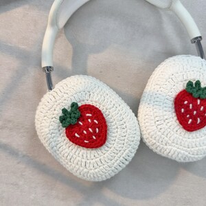 May include: White crocheted headphone covers with a red and green embroidered strawberry on each side.