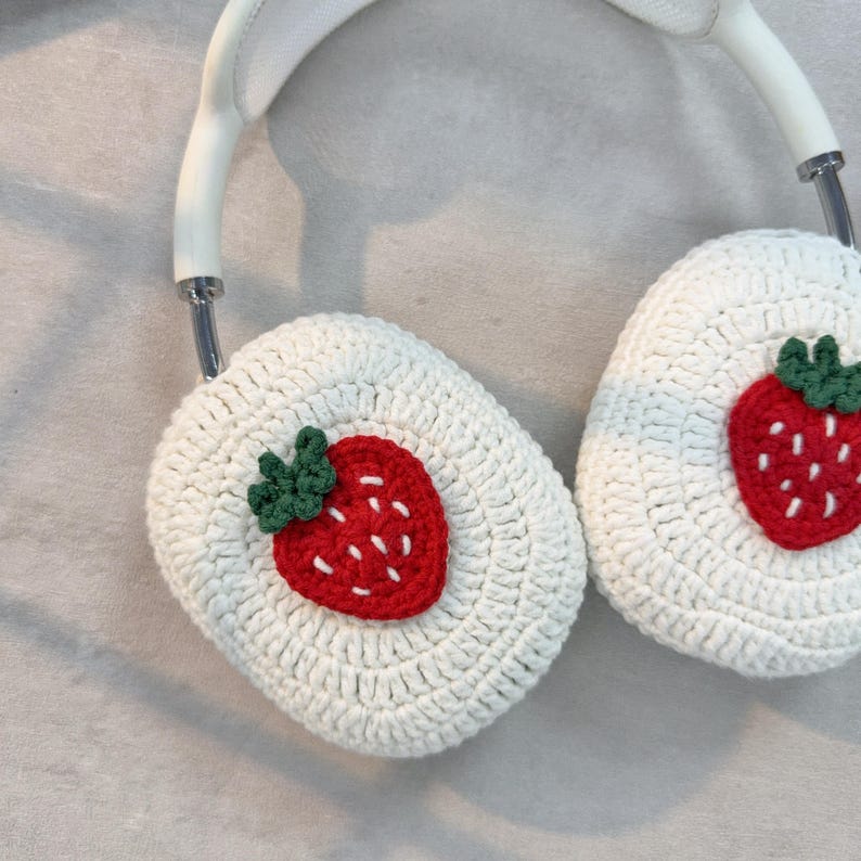 May include: White crocheted headphone covers with a red and green embroidered strawberry on each side.
