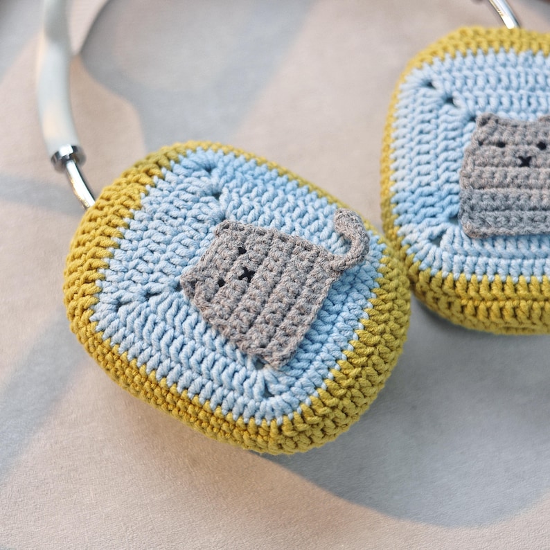 Pu&ograve; includere: Copri cuffie all'uncinetto con un design a gatto grigio. Le cover sono blu e gialle.
