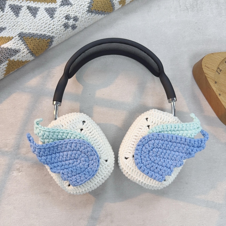 May include: White crocheted headphone covers with blue and light blue wings. The covers are attached to a black headband.