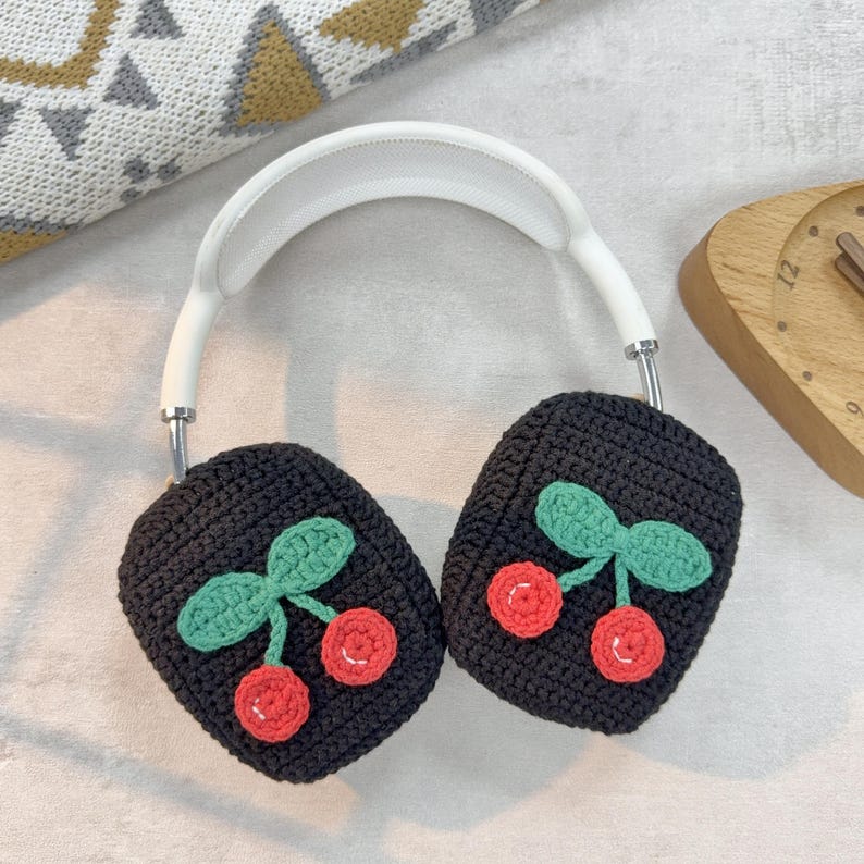 Pu&ograve; includere: Copri auricolari in maglia nera con fascia bianca. I copri auricolari presentano un motivo a ciliegie con foglie verdi e ciliegie rosse.