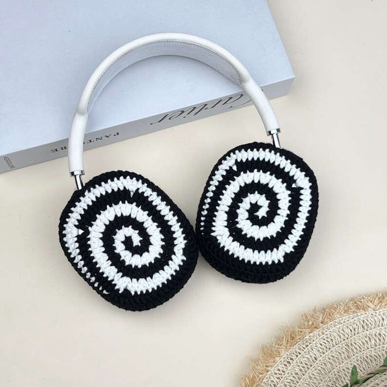 Pode incluir: Fones de ouvido brancos e prateados com capas de ouvido de croch&ecirc; em espiral em preto e branco. Os fones de ouvido t&ecirc;m uma faixa de cabe&ccedil;a branca e detalhes prateados. As capas t&ecirc;m um design de espiral conc&ecirc;ntrica.
