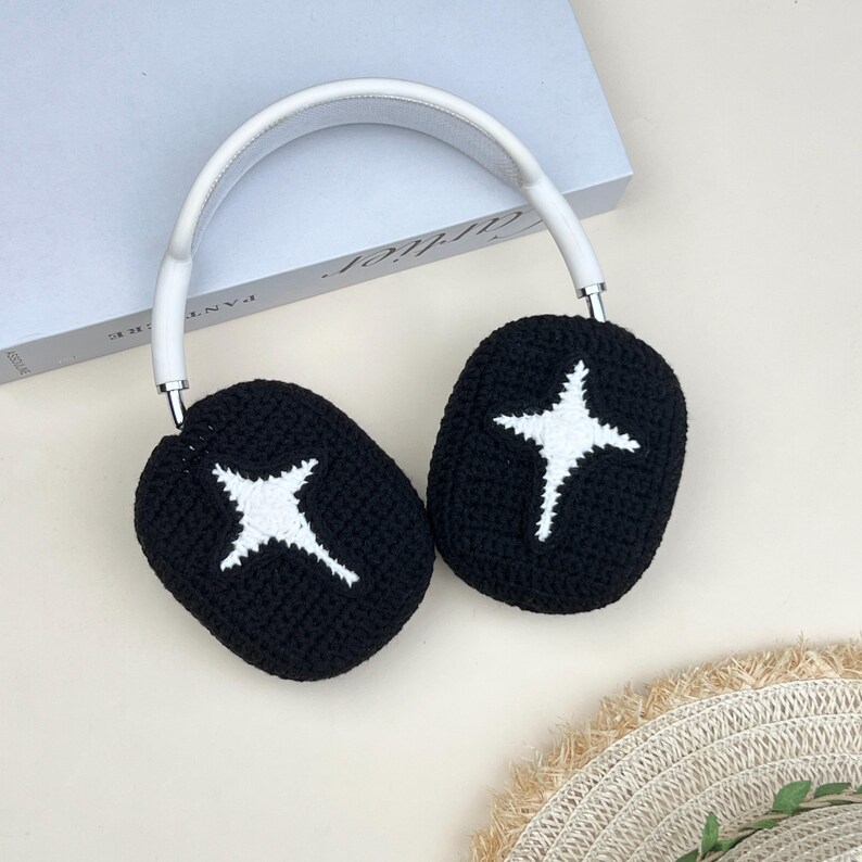 May include: White and black headphones with a star design on the earcups. The earcups are black with a white star design. The headband is white. The headphones are resting on a light-colored surface.