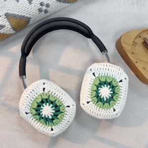 May include: White crocheted headphone covers with a green and white geometric pattern. The covers are attached to a black headband.