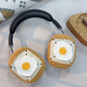 May include: Crocheted headphone covers in the shape of a fried egg. The covers are brown, white, and yellow. The headphones are black.