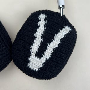 Puede incluir: Fundas de auriculares de ganchillo en blanco y negro. Las fundas son negras con un dise&ntilde;o de la letra "V" en blanco. Los auriculares tienen una diadema blanca y detalles plateados.