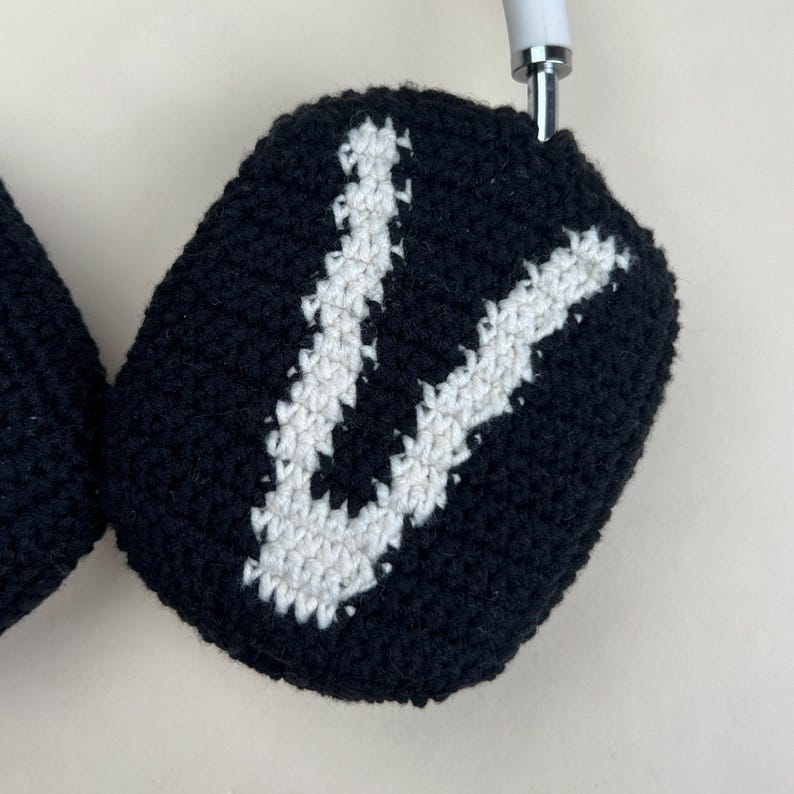 Puede incluir: Fundas de auriculares de ganchillo en blanco y negro. Las fundas son negras con un dise&ntilde;o de la letra "V" en blanco. Los auriculares tienen una diadema blanca y detalles plateados.
