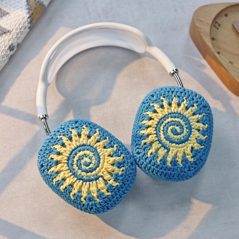 May include: White headphones with blue and yellow crocheted earmuffs featuring a sun design.