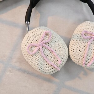 Pu&ograve; includere: Un paio di copri cuffie all'uncinetto con fiocchi rosa. Le coperture sono beige e hanno una delicata trama all'uncinetto.