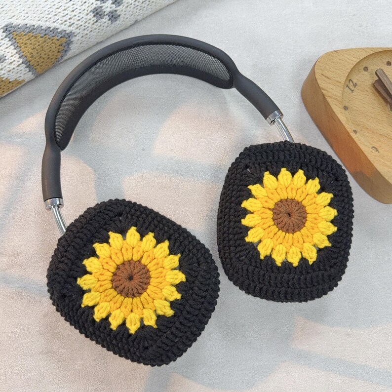 May include: Black headphones with crocheted sunflower ear covers. The ear covers are black with a yellow sunflower design.