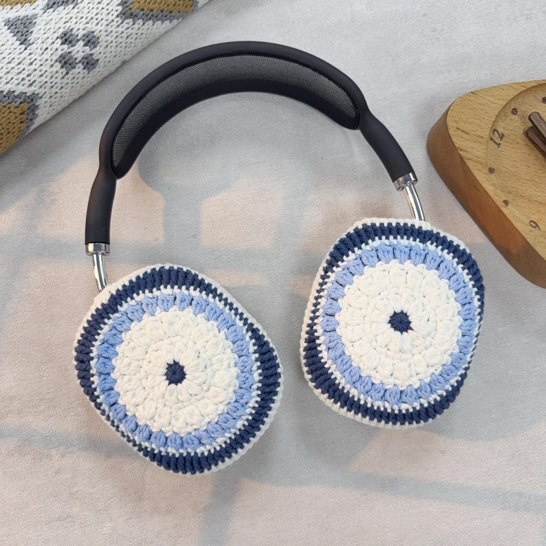 Puede incluir: Un par de orejeras de punto de ganchillo blancas, azules y azul marino para auriculares. Las orejeras son redondas y tienen un centro blanco con un borde azul y azul marino.