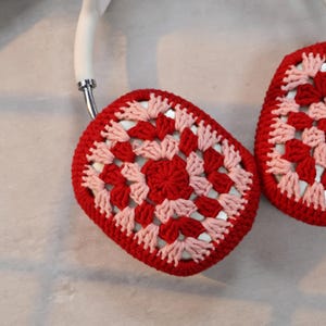 Pode incluir: Protetores de ouvido de croch&ecirc; vermelhos e rosados com uma faixa de cabe&ccedil;a branca. Os protetores de ouvido s&atilde;o feitos com um padr&atilde;o de quadrado da vov&oacute;.