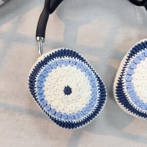 Puede incluir: Un par de orejeras de ganchillo en tonos azules y blancos. Las orejeras tienen un dise&ntilde;o circular con un centro blanco y anillos exteriores azules.