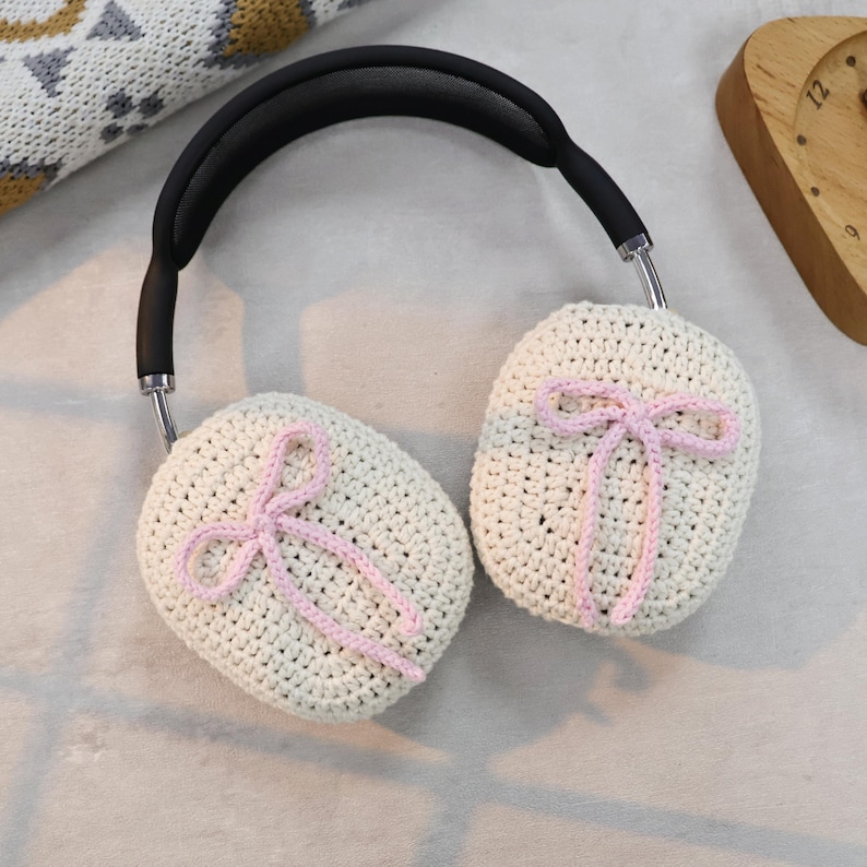 Pu&ograve; includere: Paraorecchie in crochet bianco con fiocchi rosa. I paraorecchie sono attaccati a una fascia nera.