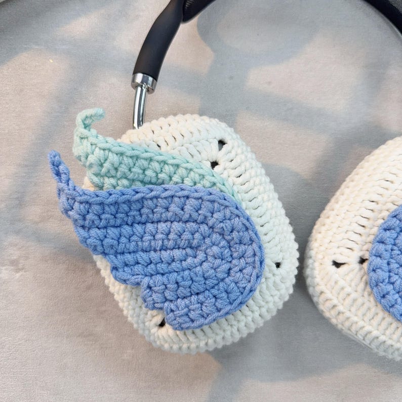 May include: Crocheted headphone covers in white, light blue, and light green. The covers feature a wing design.