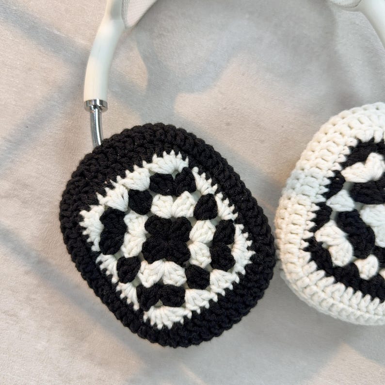 Op de afbeelding: Zwart-witte gehaakte oorwarmers met een geometrisch patroon. De oorwarmers zijn bevestigd aan een wit hoofdband.