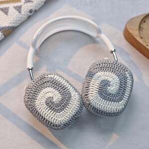 May include: White headband with grey and white crocheted earmuffs. The earmuffs have a spiral pattern.