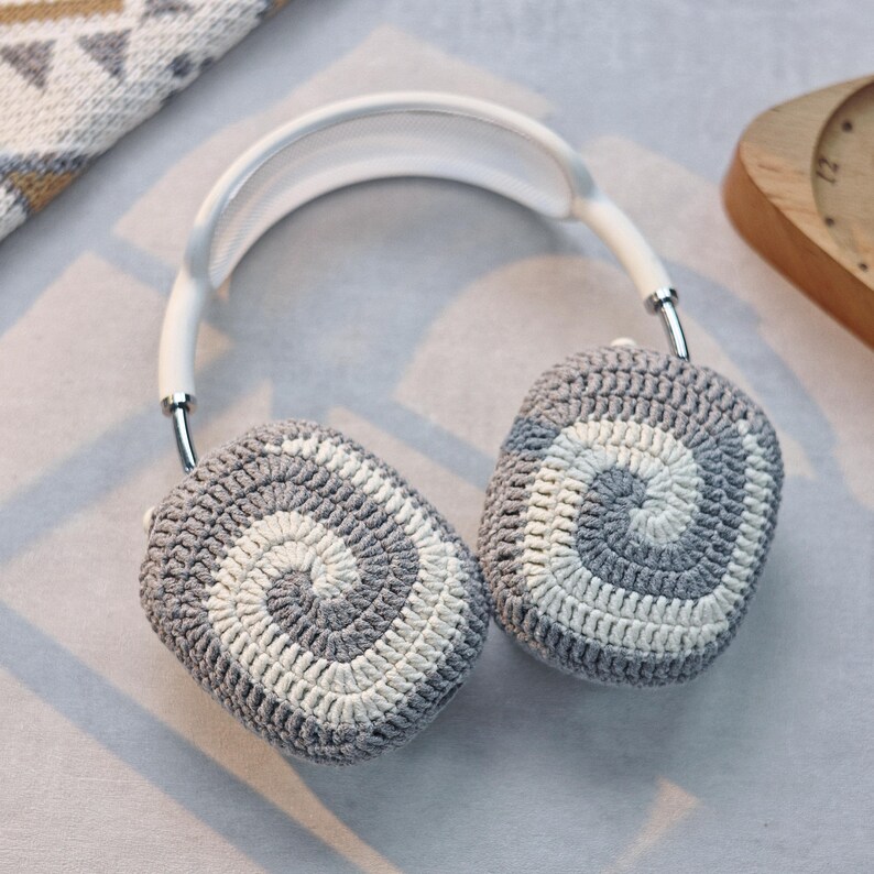 May include: White headband with grey and white crocheted earmuffs. The earmuffs have a spiral pattern.