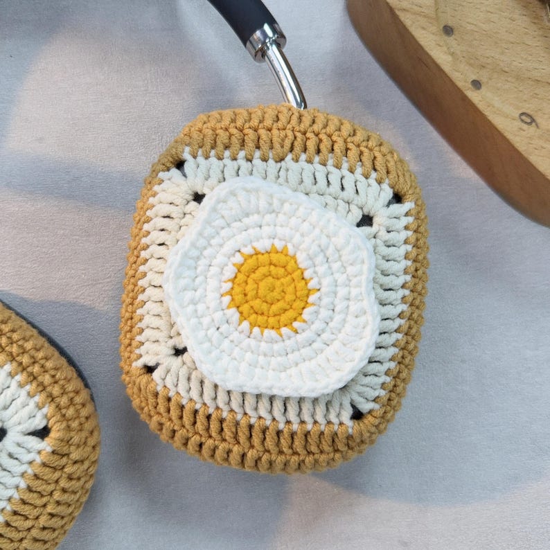 May include: A crocheted headphone cover with a yellow and white egg design. The cover is made of a soft, textured yarn and is perfect for protecting your headphones from dust and scratches.