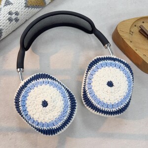 Puede incluir: Un par de auriculares con cubiertas de orejas de ganchillo. Las cubiertas de las orejas son blancas con rayas azules y azul marino.