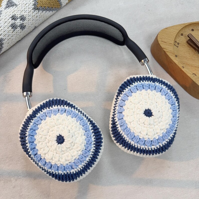 Puede incluir: Un par de auriculares con cubiertas de orejas de ganchillo. Las cubiertas de las orejas son blancas con rayas azules y azul marino.