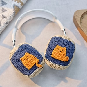 May include: White headphones with crocheted earmuffs featuring a yellow cat design. The earmuffs are blue and beige.