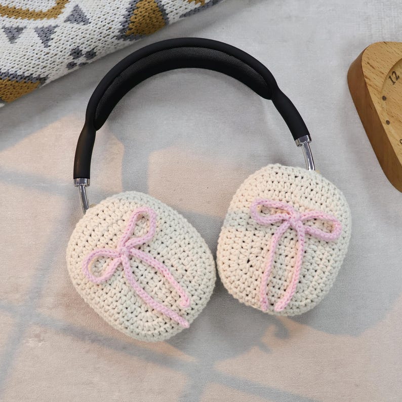 Pu&ograve; includere: Paraorecchie in crochet bianco con fiocchi rosa. I paraorecchie sono attaccati a una fascia nera.