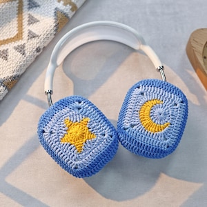 Puede incluir: Cubiertas para auriculares de crochet azul con un dise&ntilde;o de estrella amarilla y luna creciente.