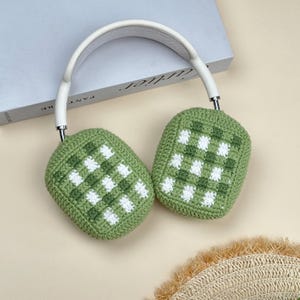 May include: White and silver headphones with green and white checkered crochet ear covers. The headphones have a white headband and silver accents. The ear covers are a light green color with white squares.