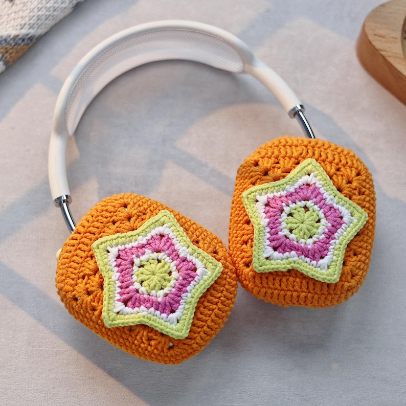 May include: Orange crocheted headphone covers with a white headband. Each cover features a multi-colored star with pink, green, and white yarn.