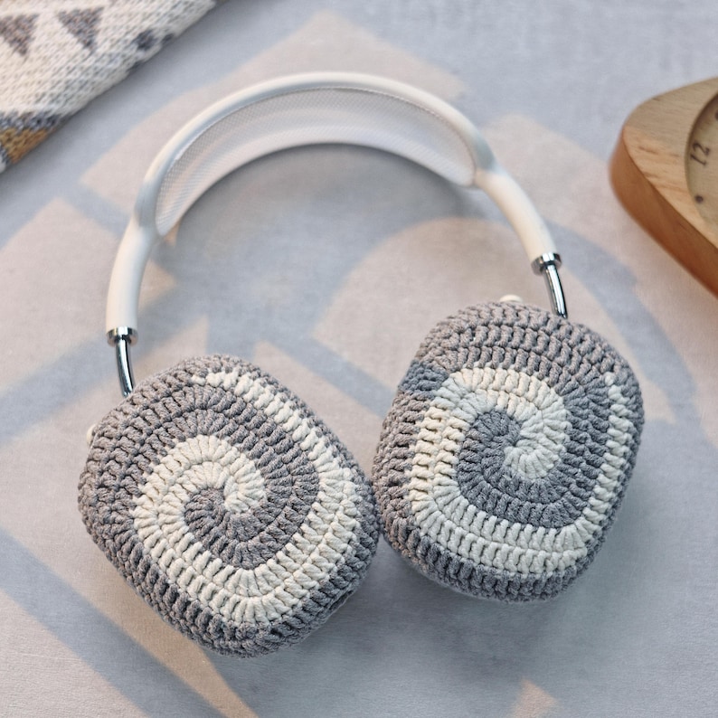 May include: White headphones with grey and white crocheted ear covers. The ear covers have a spiral pattern.