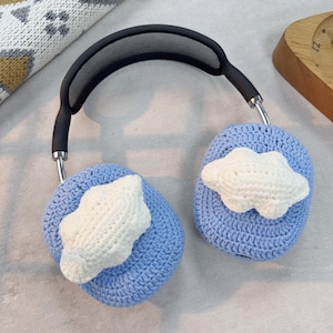May include: Blue crocheted headphone covers with white crocheted cloud designs. The covers are attached to a black headband with a mesh design.