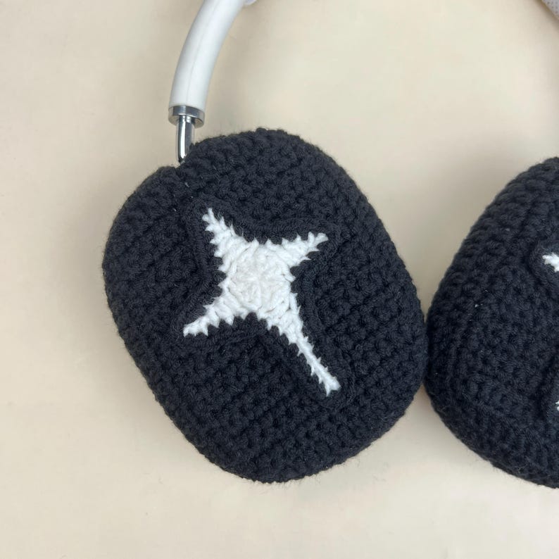 May include: Black crochet headphone covers with a white starburst design. The covers are designed to fit over the earcups of a white headset. The crochet work is visible, showing the texture of the yarn.