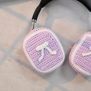 May include: A pair of purple crocheted headphone covers with a white crocheted border and a white pi symbol on each cover.