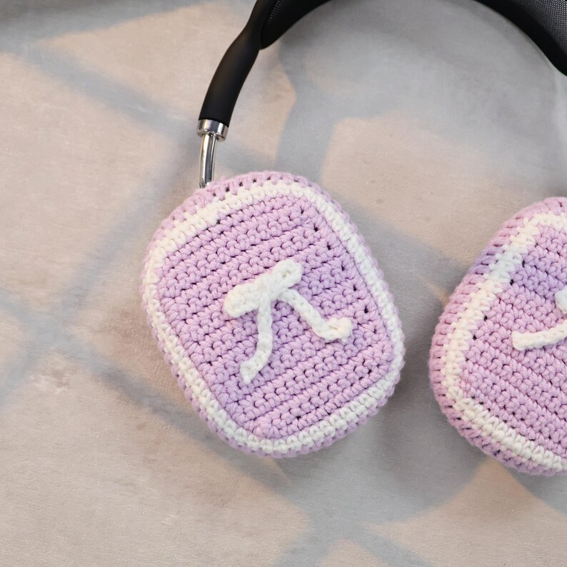May include: A pair of purple crocheted headphone covers with a white crocheted border and a white pi symbol on each cover.
