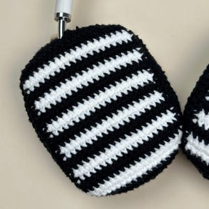 May include: Handmade crochet headphone covers with a black and white striped design. The covers are crafted with a contrasting pattern of black and white stripes. The design is a classic black and white, with evenly spaced stripes. The covers are designed to fit over the ear cups of headphones.