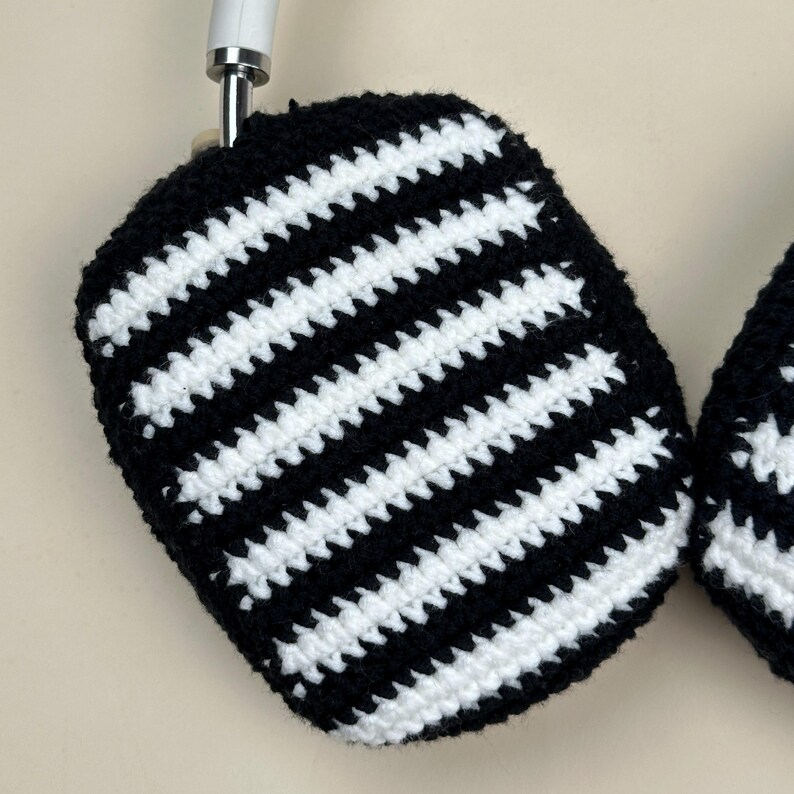 May include: Handmade crochet headphone covers with a black and white striped design. The covers are crafted with a contrasting pattern of black and white stripes. The design is a classic black and white, with evenly spaced stripes. The covers are designed to fit over the ear cups of headphones.