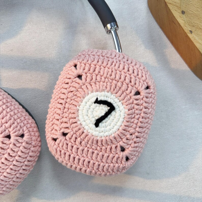 K&ouml;nnte beinhalten: Rosa gestrickte Kopfh&ouml;rerbez&uuml;ge mit einem wei&szlig;en Kreis und der schwarzen Zahl 7 in der Mitte.