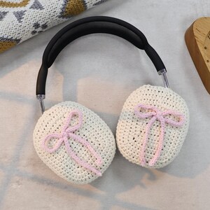 Pu&ograve; includere: Paraorecchie in crochet bianco con fiocchi rosa. I paraorecchie sono attaccati a una fascia nera.