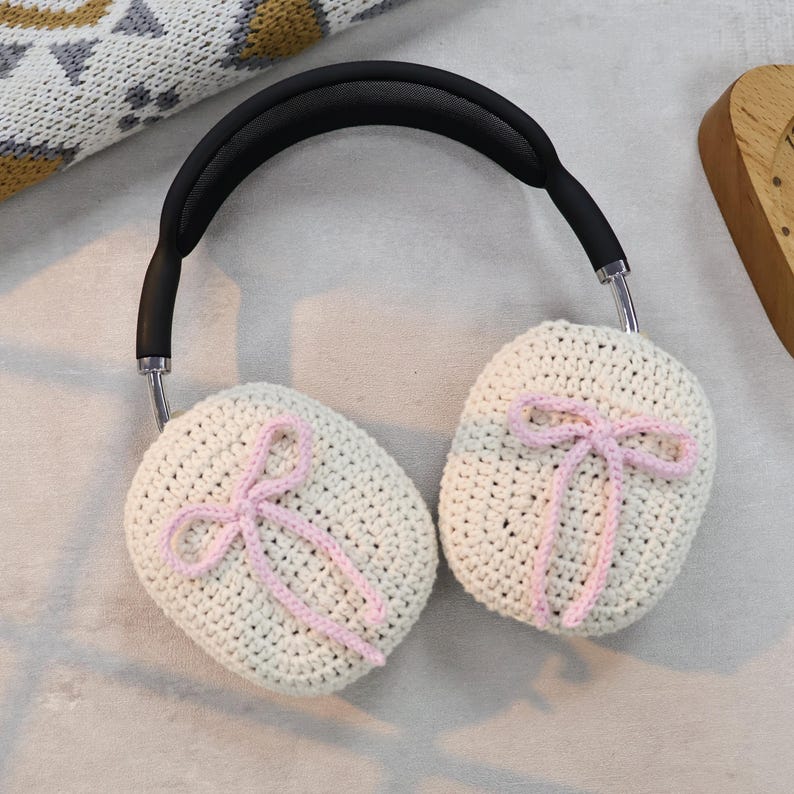 Pu&ograve; includere: Paraorecchie in crochet bianco con fiocchi rosa. I paraorecchie sono attaccati a una fascia nera.