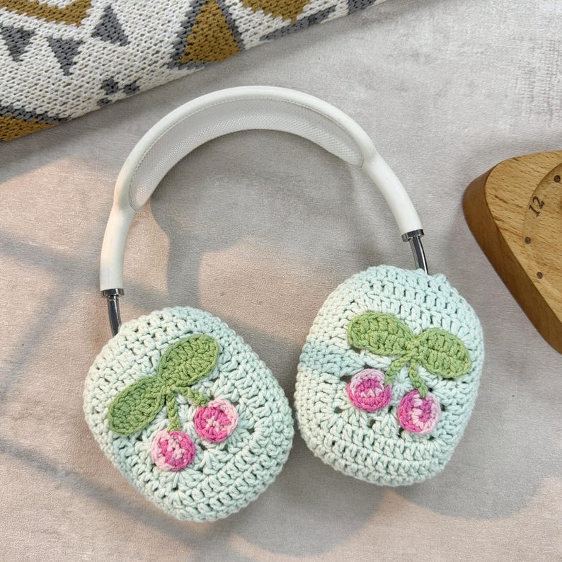 Pu&ograve; includere: Un paio di cuffie bianche con paraorecchie all'uncinetto. I paraorecchie sono di colore verde chiaro con ciliegie rosa e verdi ricamate.