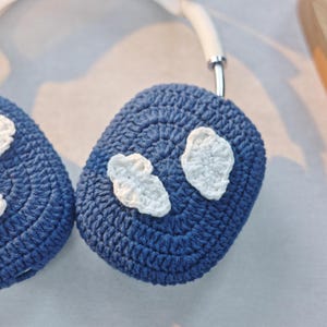 May include: A pair of blue crocheted headphone covers with white crocheted cloud designs.