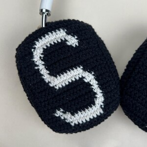 Puede incluir: Fundas de auriculares de ganchillo negras con un dise&ntilde;o de letra "S" blanca. Las fundas est&aacute;n hechas a mano y parecen estar hechas de hilo suave. Los auriculares tienen una diadema blanca.