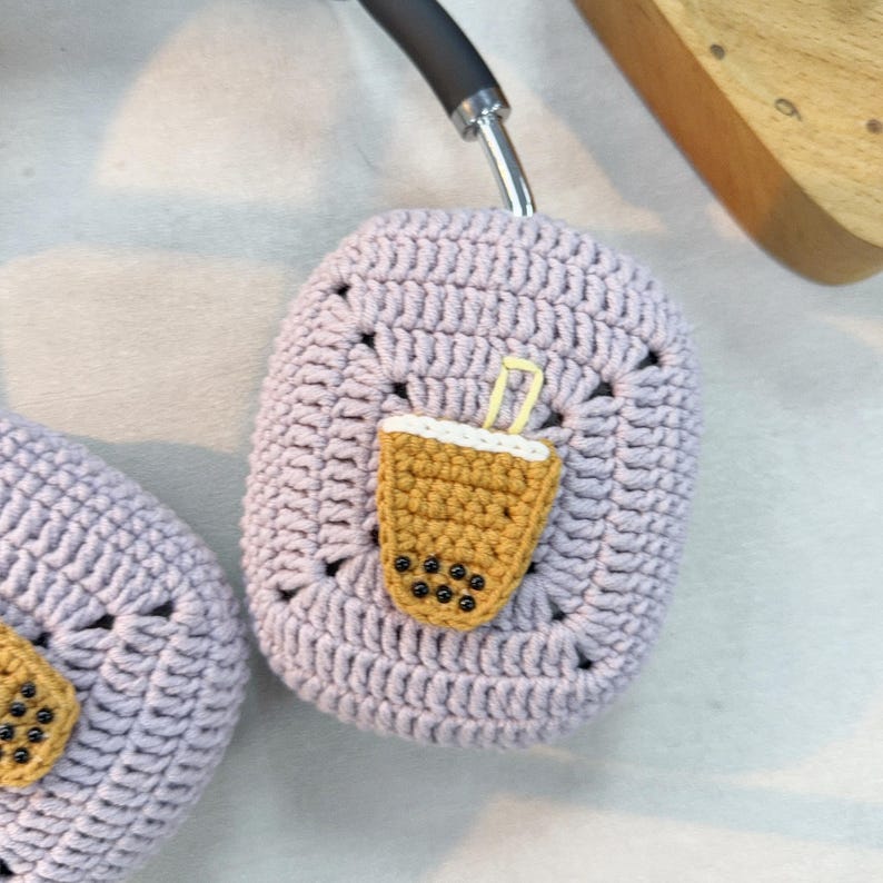 May include: A pair of lavender crocheted headphone covers with a crocheted boba tea design. The boba tea is yellow with black boba pearls.